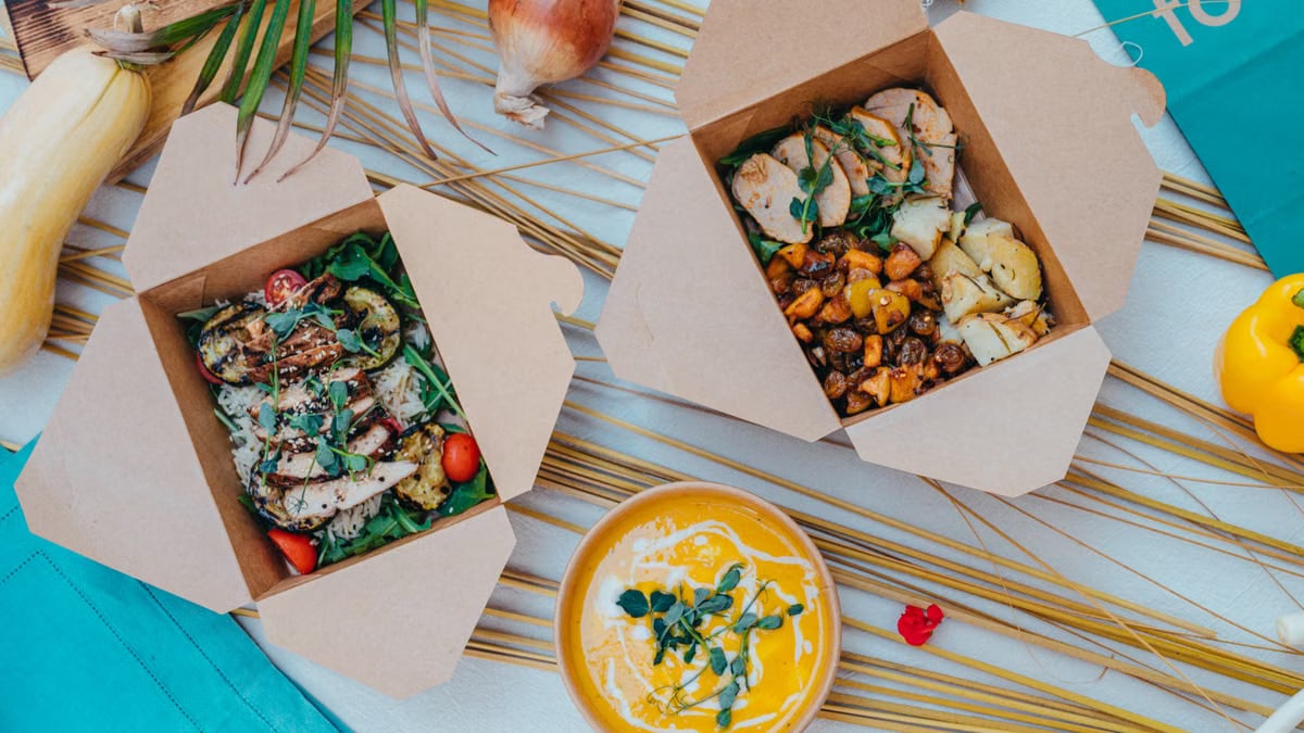 Top view of healthy takeout boxes with salad and soup on a colorful background.