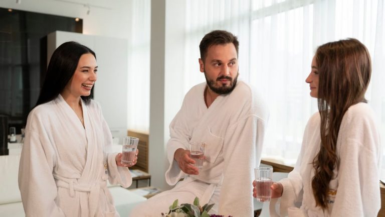 Three adults enjoying a relaxing spa day, chatting and drinking water indoors.